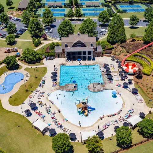 Aerial view of a recreational park featuring pools, water slides, tennis courts, playground, and a clubhouse on a sunny day.
