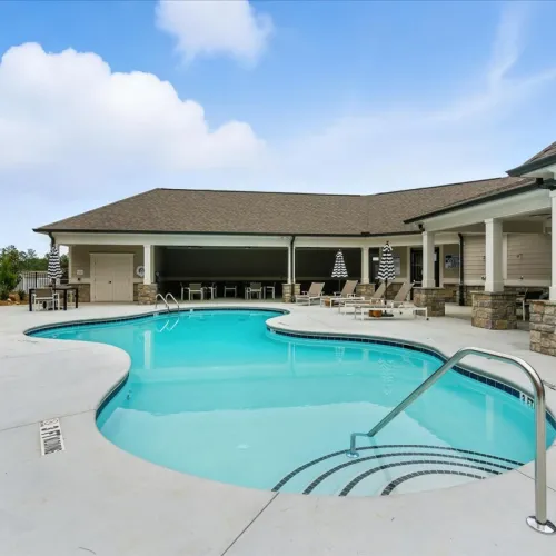 Outdoor swimming pool with lounge chairs and umbrellas by a covered patio under a clear blue sky.