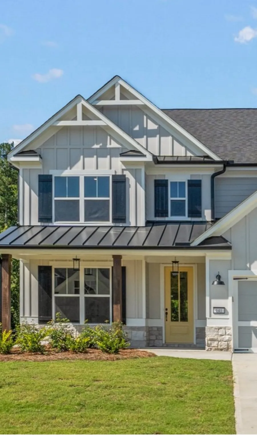 Modern two-story house with white siding, black shutters, yellow front door, and a manicured green lawn.
